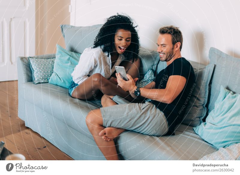 Happy young couple relaxed at home in the couch reading a book and looking at the mobile phone interracial Relationship Couple Youth (Young adults) Book Reading