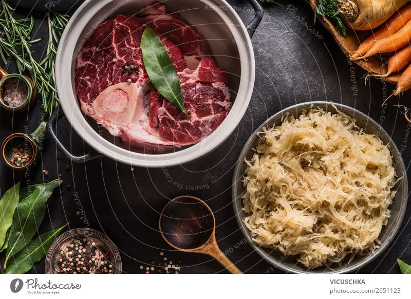 Ingredients for low carb pickled cabbage  and beef meat stew or soup. Raw beef meat shin with bone in cooking pot with spices and bowl with pickled cabbage on dark kitchen tables background