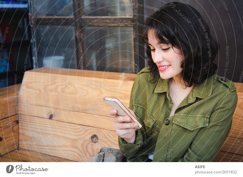 Smiling young woman using her smart phone at a cafe bar Lifestyle Happy Beautiful Leisure and hobbies Blackboard Telephone Cellphone PDA Technology Woman Adults