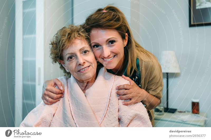 Female caretaker posing with elderly patient Happy Health care Illness Lamp Bedroom Doctor Hospital Human being Woman Adults Old Smiling Sit Embrace Authentic