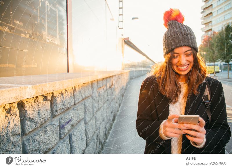 Happy young woman with her mobile on the street Lifestyle Joy Beautiful Reading Sun Winter Telephone PDA Technology Internet Woman Adults Youth (Young adults)