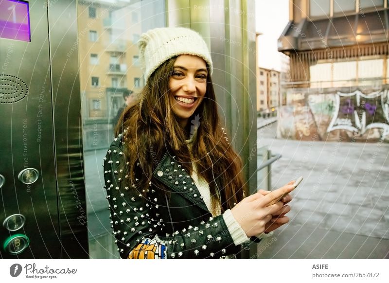 Urban young woman using phone on elevator Lifestyle Joy Happy Beautiful Reading Winter Telephone PDA Technology Internet Woman Adults Youth (Young adults) Hand