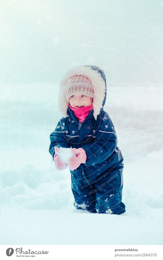 Happy little girl enjoying snow. Child playing outdoors walking through deep snow in wintertime while snow falling. Toddler is wearing dark blue snowsuit