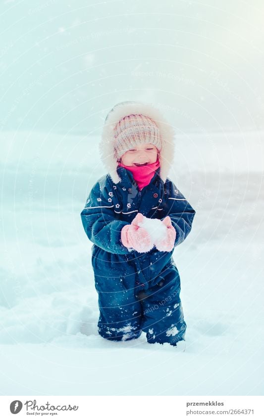 Happy little girl enjoying snow. Child playing outdoors walking through deep snow in wintertime while snow falling. Toddler is wearing dark blue snowsuit