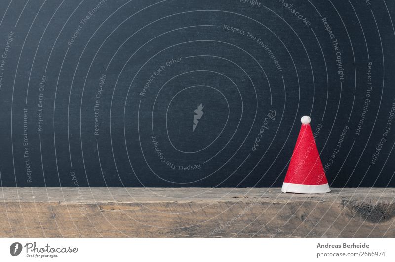 Santa Claus cap on a wooden board in front of a blackboard Winter Christmas & Advent Blackboard Hat Cap Decoration Tradition decor Symbols and metaphors concept