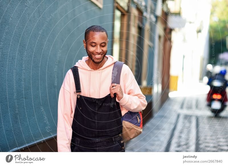 Black young man with arms crossed smiling in urban background - a ...