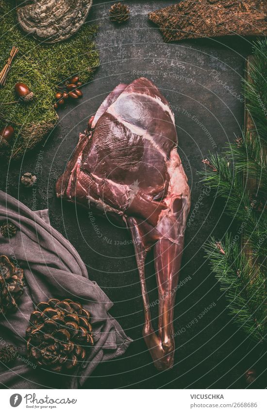 Raw aged leg of venison with bone on dark kitchen table background , top view. Raw meat leg of deer. Cooking preparation of venison roast raw cooking haunch