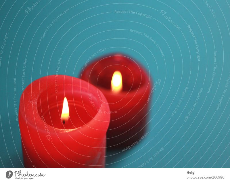 two red burning candles stand one behind the other in front of a turquoise background Decoration shoulder stand Flame Wick Wax Illuminate Stand