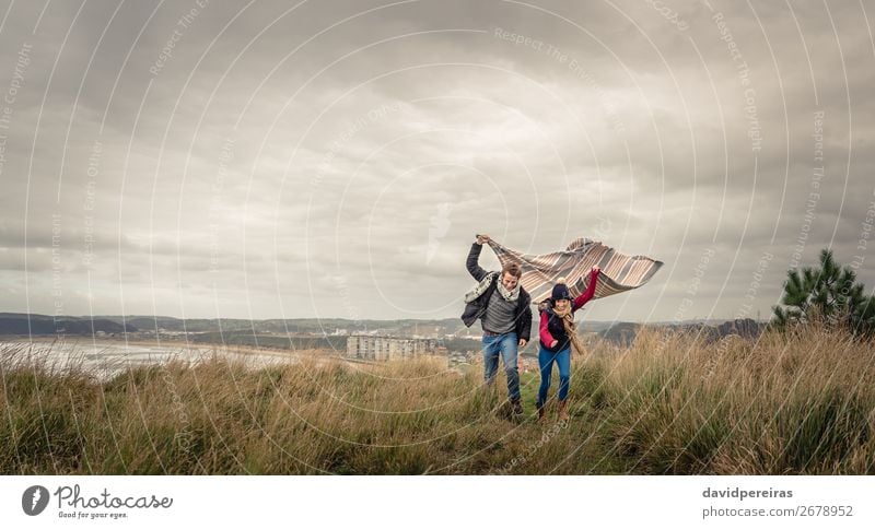 Young couple playing outdoors with blanket in a windy day Lifestyle Joy Happy Beautiful Playing Ocean Winter Mountain Woman Adults Man Couple Nature Sky Clouds