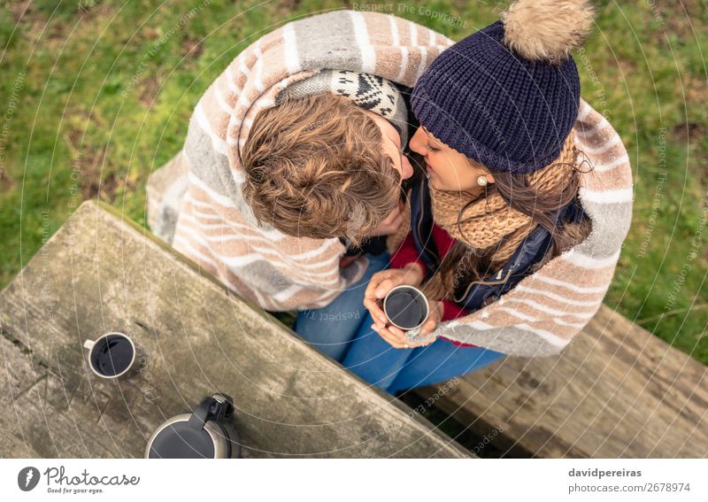 Young couple under blanket with hot drink kissing outdoors Beverage Coffee Tea Lifestyle Happy Winter Table Woman Adults Man Couple Hand Nature Autumn Wind
