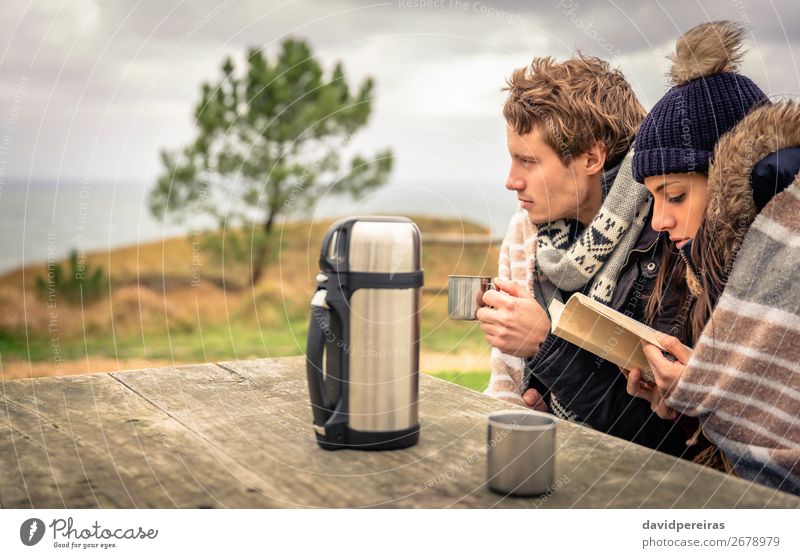 Young couple in a cold day with cloudy sky on the background Beverage Coffee Tea Lifestyle Happy Reading Ocean Winter Table Woman Adults Man Couple Hand Book