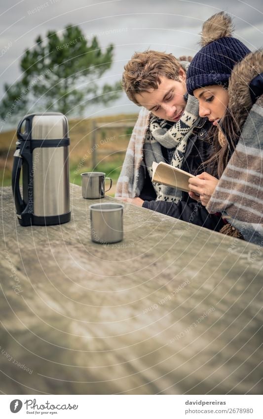 Young couple under blanket reading book outdoors in a cold day Beverage Coffee Tea Lifestyle Reading Adventure Winter Mountain Table Woman Adults Man Couple