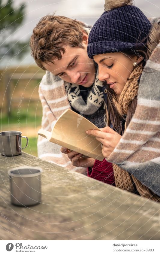 Young couple under blanket reading book outdoors in a cold day Beverage Coffee Tea Lifestyle Happy Reading Ocean Winter Mountain Table Woman Adults Man Couple