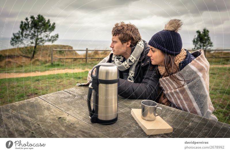 Young couple under blanket looking the sea in a cold day Beverage Coffee Tea Lifestyle Happy Ocean Winter Mountain Table Woman Adults Man Couple Nature Sky