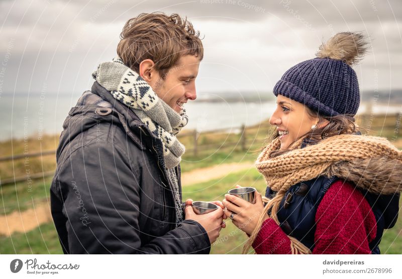 Young couple holding cups of hot drink outdoors in a cold day Beverage Coffee Tea Lifestyle Happy Ocean Winter Mountain Woman Adults Man Couple Hand Nature Sky