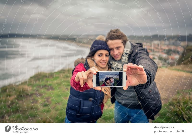 Young couple taking selfie photo with smartphone outdoors Happy Adventure Beach Ocean Winter Telephone PDA Woman Adults Man Couple Nature Landscape Sky Clouds