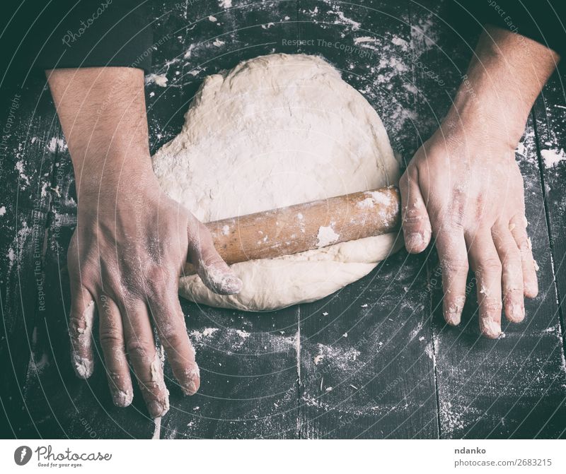 chef in a black tunic rolls a dough for a round pizza Dough Baked goods Bread Nutrition Table Kitchen Human being Man Adults Hand Wood Make Fresh Black White