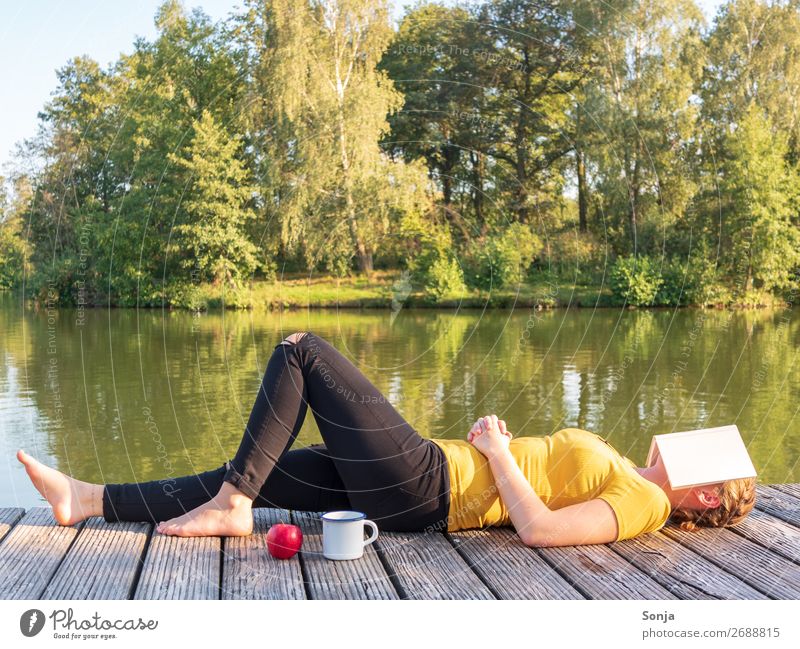 Woman with a book on her face lies by the lake Lifestyle Freedom Summer Sunbathing Human being Feminine Young woman Youth (Young adults) 1 18 - 30 years Adults