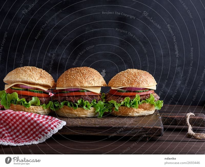 three hamburgers with vegetables Meat Cheese Vegetable Bread Roll Lunch Dinner Fast food Table Blackboard Wood Dark Fresh Red Salad American background bbq Beef