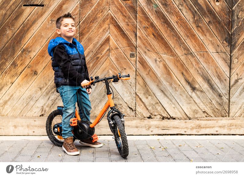 Litle boy with a bike on a wooden door background Lifestyle Joy Happy Beautiful Face Leisure and hobbies Playing Vacation & Travel Trip City trip