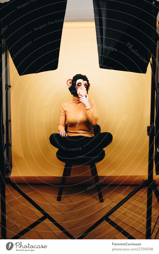 Woman with monkey mask sitting thoughtfully in photo studio Feminine Adults 1 Human being 18 - 30 years Youth (Young adults) 30 - 45 years Joy Monkeys