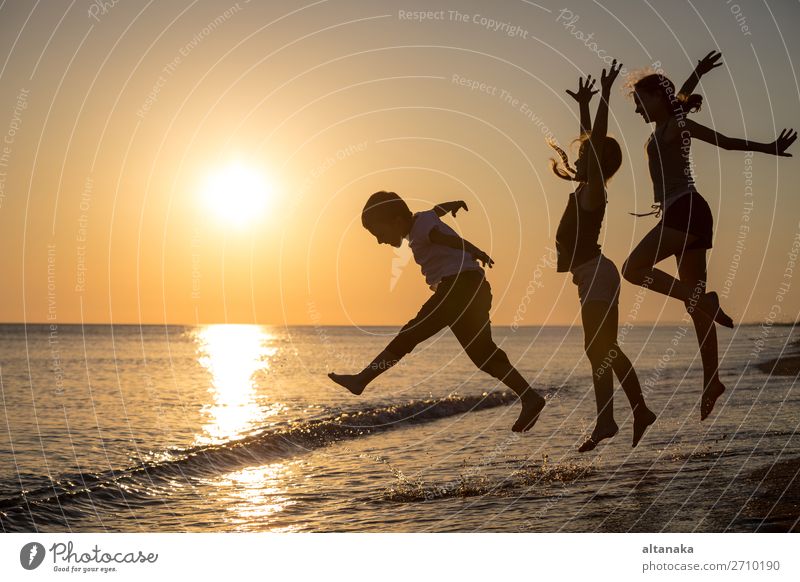 Happy children playing on the beach at the sunset time. Three Kids having fun outdoors. Concept of summer vacation and friendly family. Lifestyle Joy