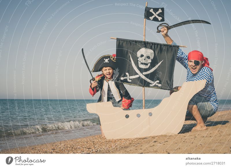 Father and son playing on the beach at the day time. They are dressed in sailor's vests and pirate costumes. Concept of happy game on vacation and friendly family.