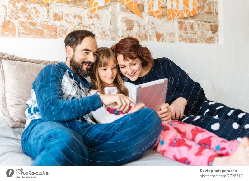 Couple relaxed at home in bed with their little daughter on the mobile phone and tablet Affection Bed Bedroom Wife Husband Daughter Child Mobile Telephone