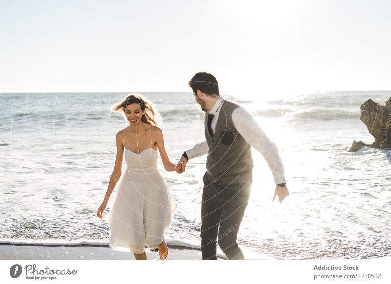 Beautiful bridal couple running on shore Couple Running Beach Happiness seaside holding hands Cheerful Exterior shot Together Contentment Summer Dress Wedding