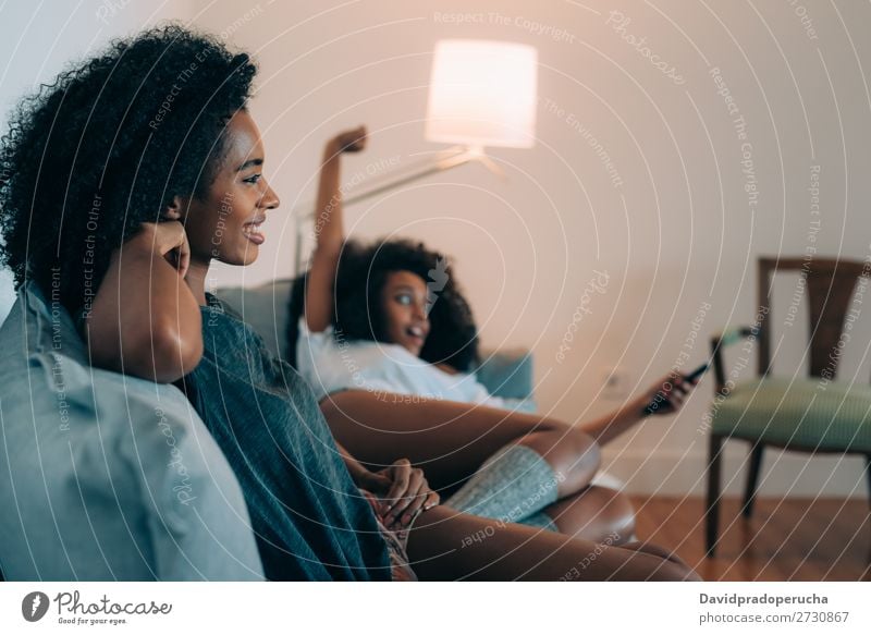 Happy young two black women lying down in the couch watching tv Woman Television Technology Observe modern relationship Home Beauty Photography pretty American