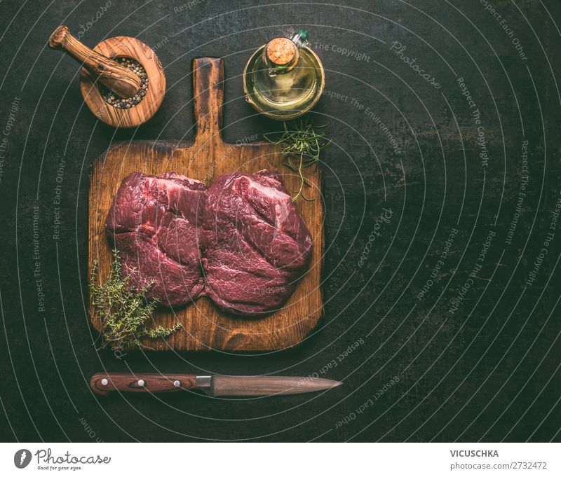 Raw marble beef meat on wooden cutting board with herbs,spices , oil and knife on dark rustic background, top view. Copy space for your design or cooking recipes