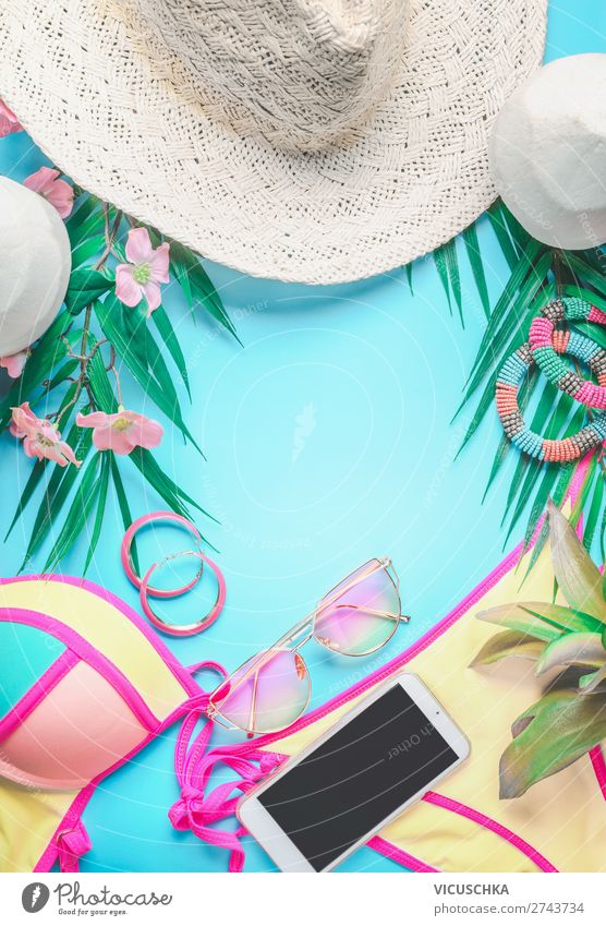 Top view of female beach accessories  background with tropical leaves and flowers , sunglasses and straw hat, bikini and smartphone on sunny blue. Summer holiday concept
