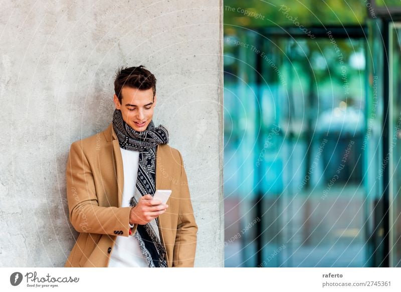 Front view of fashionable young man wearing denim clothes leaning on a wall while using a mobile phone outdoors Lifestyle Elegant Style Beautiful