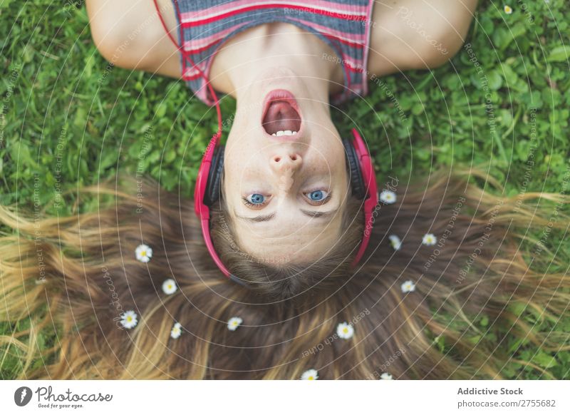 Excited girl in headphones on grass Woman Expressive Headphones Posture Grass Lie (Untruth) Park facial Flower Excitement Model mouth opened Expression Style