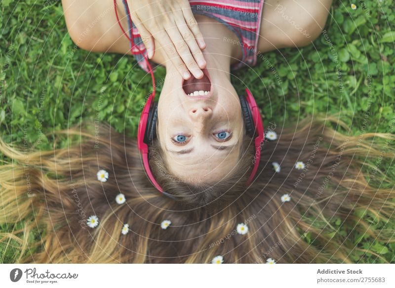 Excited girl in headphones on grass Woman Expressive Headphones Posture Grass Lie (Untruth) Park facial Flower Excitement Model mouth opened Expression Style
