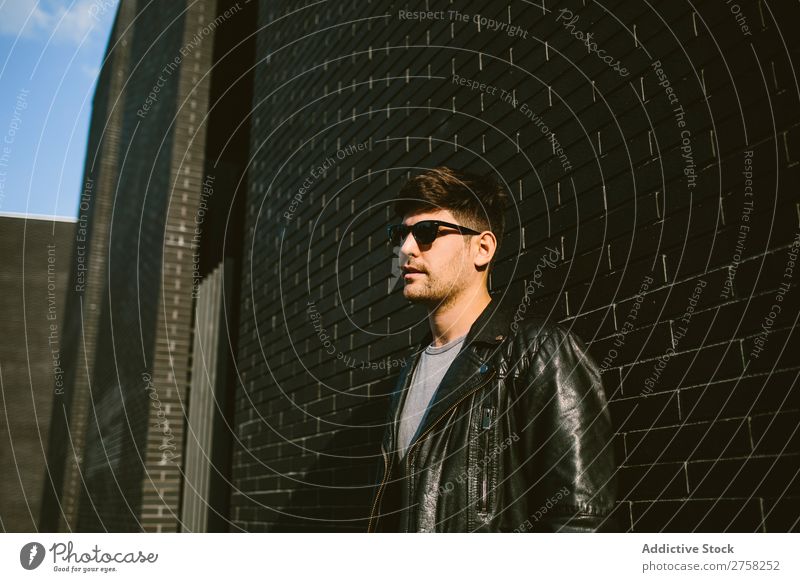 Young handsome man over a dark brick wall serious sunglasses confident young cool person portrait modern model fashionable male casual guy adult caucasian
