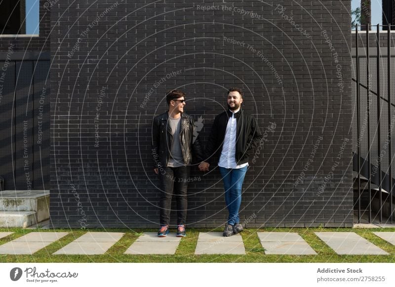 Alternative couple at brick wall standing holding hands looking at camera posing gay homosexual pair male love two together lifestyle relationship young men