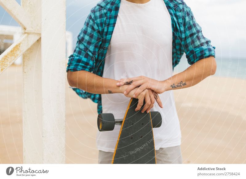 Man in summer apparel holding skateboard on sandy beach. Skateboard Coast Beach Leisure and hobbies Summer Multicoloured youngster Action Youth (Young adults)