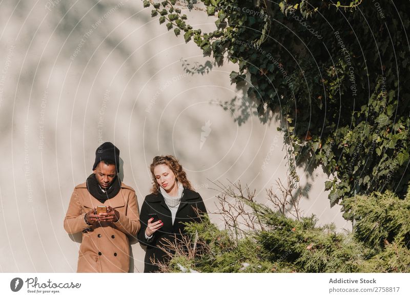 Couple in warm clothes with smartphones multiethnic Style Street PDA using Stand Easygoing Beautiful Mixed race ethnicity Black Youth (Young adults) Together