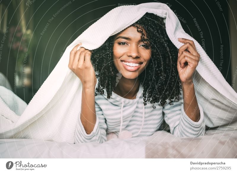 close up of a pretty black woman with curly hair smiling and covering with sheets on bed looking at the camera Woman Bed Sheet Portrait photograph Close-up