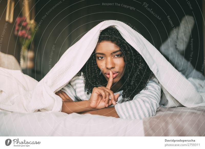 attractive black woman asking for silence with finger on lips on bed Fingers Lips Beautiful Face Mysterious Gesture Woman Bed Portrait photograph Close-up