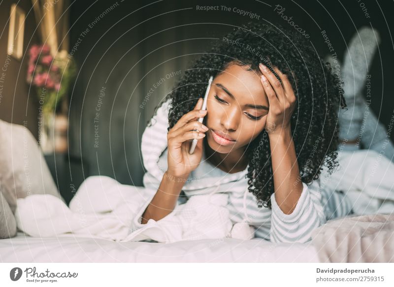 Beautiful serious thoughtful and sad black woman with curly hair using smartphone on bed Woman Bed Mobile Telephone PDA looking down Sadness Anger Black worried