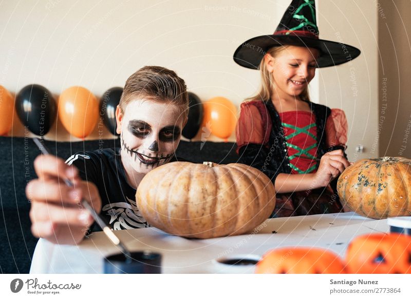 Happy children disguised decorating a pumpkin at home. Hallowe'en Child Girl Boy (child) Painting (action, artwork) Skeleton Witch Disguised Joy