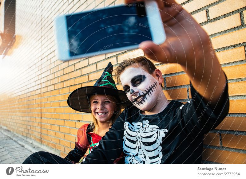 Happy children disguised taking photo with phone in the street. Hallowe'en Child Girl Boy (child) Selfie Skeleton Disguised Mobile PDA Photography Telephone