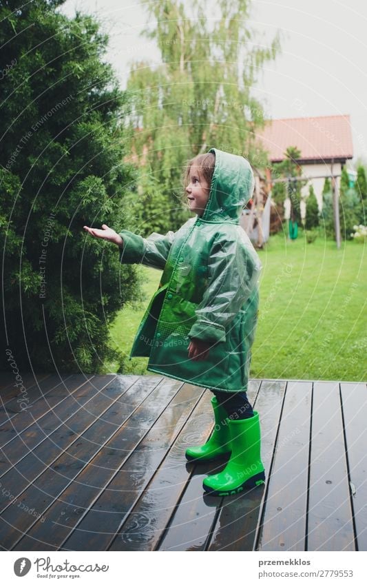 Little girl standing on rain wearing green raincoat Lifestyle Joy Happy Summer Child Human being Woman Adults Infancy Weather Rain Coat Boots Rubber boots