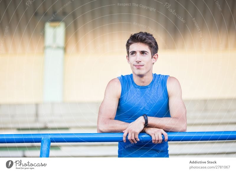 Young man in sportswear leaning on metal fence and posing on sta Man Stadium Athletic Posture Rest sportsman Sports Fitness Contentment Practice Lean Athlete