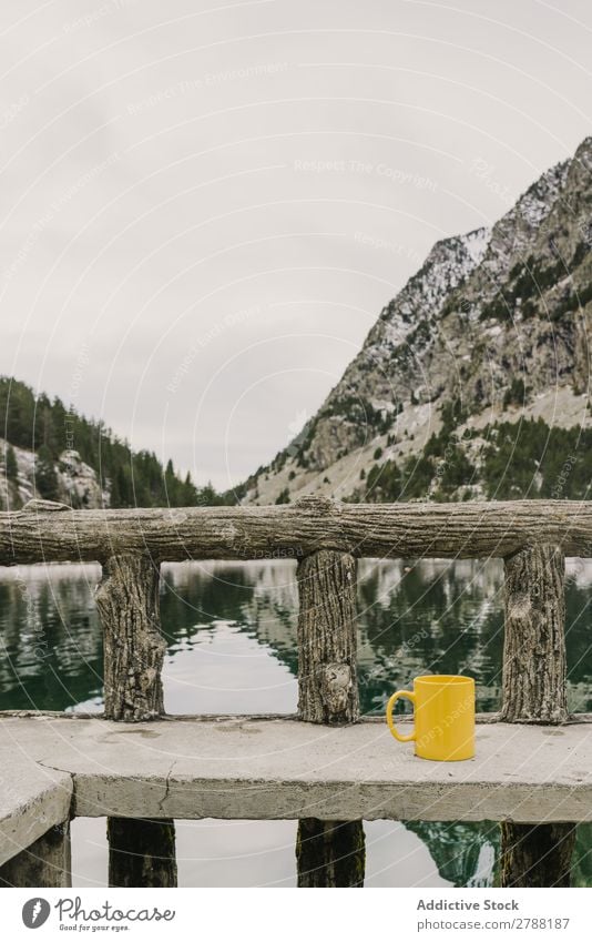 Cup on seat near wonderful lake between hills in snow and cloudy sky Lake Hill Seat Snow Pyrenees Sky Wonderful Water Surface Mountain Mug Yellow Clouds Height