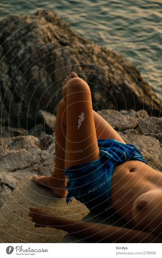 Young bare-breasted woman with a cloth around her loins lies lasciviously on a rock on the Adriatic coast in the evening Lifestyle Exotic Summer vacation