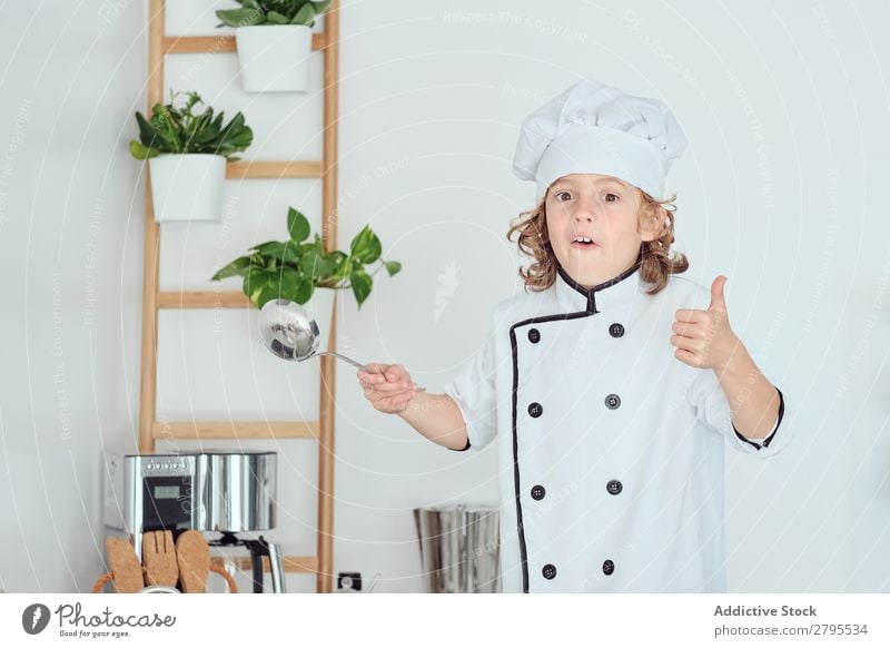 Boy in cook hat holding ladle and showing thumb up in kitchen Cook Boy (child) Kitchen Ladle chef Child Hat Cool (slang) Gesture Cooking Metal Modern Home