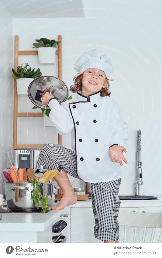 Boy in cook hat with cover near pot on chair in kitchen Cook Boy (child) Pot Cover Kitchen Chair chef Child Vegetable Hat Cooking Modern Funny Home Light